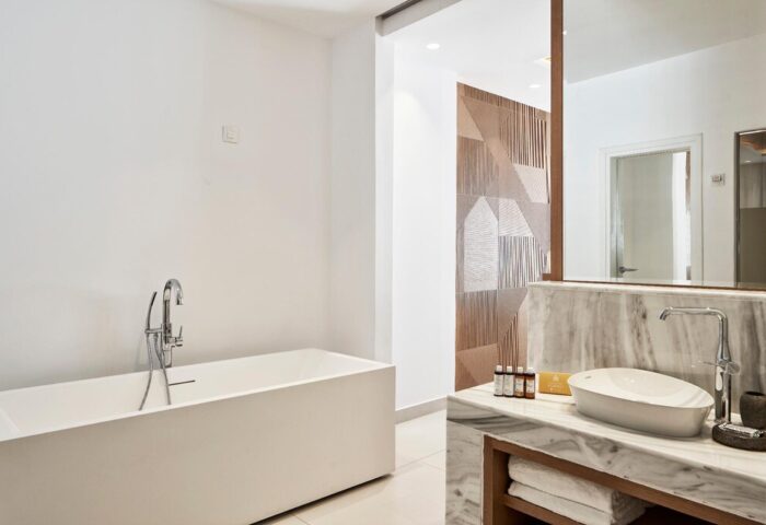 Myconian Korali Relais and Chateaux gay-friendly hotel bathroom. Bathtub, marble vanity, and geometric wall art. Luxury Mykonos travel.