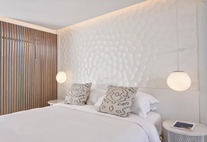 Myconian Kyma Design Hotel bedroom. Gay-friendly hotel room with white textured wall, bed, pillows, and bedside lamps. Mykonos travel.
