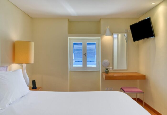 Mykonos Theoxenia gay-friendly hotel room. Interior view of a bedroom with a bed, window, TV, and vanity. Modern design for gay travel.
