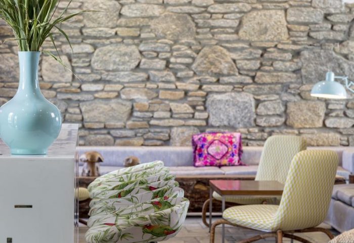 Mykonos Theoxenia gay-friendly hotel interior. Stone wall, stylish chairs, and a blue vase create a chic, welcoming atmosphere.