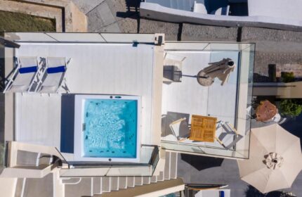 Aerial view of Mythical Blue Luxury Suites' gay-friendly hotel. Features a jacuzzi, lounge chairs, and outdoor seating in Santorini.