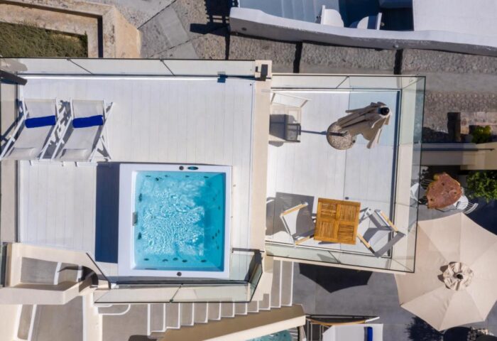 Aerial view of Mythical Blue Luxury Suites' gay-friendly hotel. Features a jacuzzi, lounge chairs, and outdoor seating in Santorini.