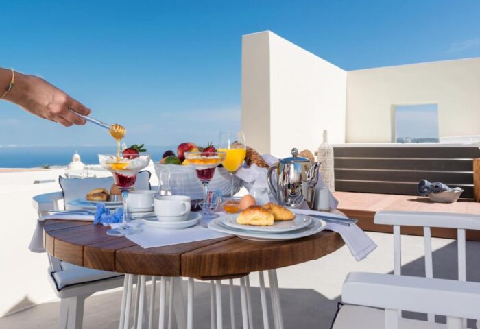 Breakfast at Mythical Blue Luxury Suites, a gay-friendly hotel. Honey being poured over fruit and yogurt. Ocean view. Santorini luxury.