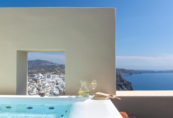 Mythical Blue Luxury Suites gay-friendly hotel view. Santorini caldera, jug, book, & jacuzzi. Perfect gay travel getaway.