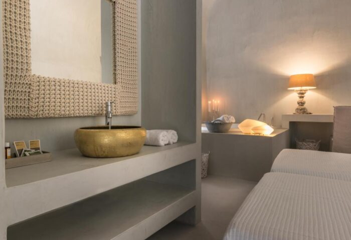Bathroom at Mythical Blue Luxury Suites, a gay-friendly hotel. Gold sink, woven mirror frame, and soft lighting create a relaxing ambiance.