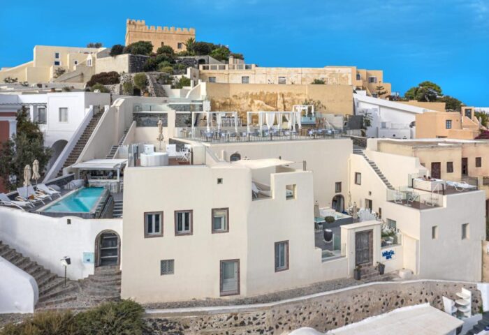 Mythical Blue Luxury Suites, a gay-friendly hotel. Whitewashed buildings with pool, rooftop dining, and castle in Santorini, Greece.