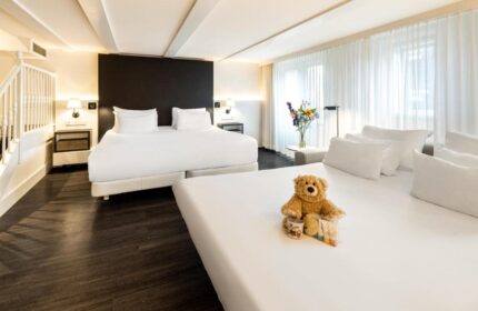 NH Collection Amsterdam Barbizon Palace room. Gay-friendly hotel features plush beds, modern decor, and a welcoming teddy bear. Luxury stay.