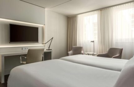 NH Collection Amsterdam Barbizon Palace gay-friendly hotel room. Twin beds, desk, TV, chairs, and bright windows. Modern design.