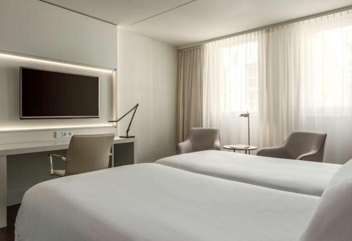 NH Collection Amsterdam Barbizon Palace gay-friendly hotel room. Twin beds, desk, TV, chairs, and bright windows. Modern design.