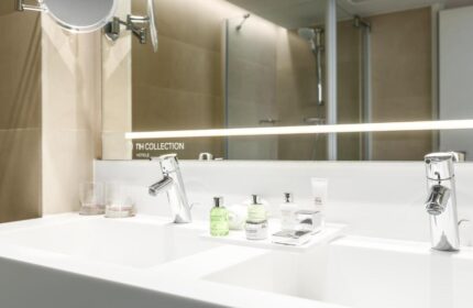 Bathroom detail at NH Collection Amsterdam Barbizon Palace, a gay-friendly hotel. Double sink, toiletries, mirror, and shower in the background.