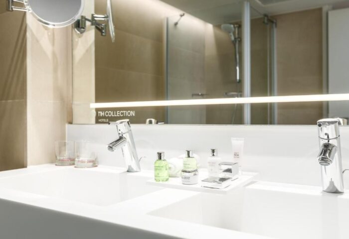 Bathroom detail at NH Collection Amsterdam Barbizon Palace, a gay-friendly hotel. Double sink, toiletries, mirror, and shower in the background.