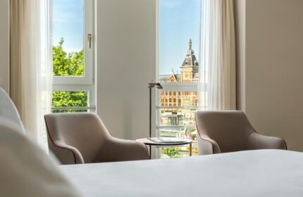 NH Collection Amsterdam Barbizon Palace room view. Two chairs face a window overlooking Amsterdam's architecture. Gay-friendly hotel.