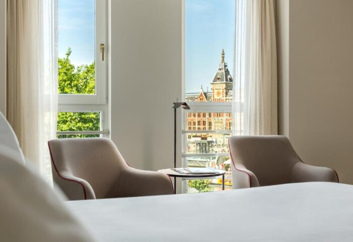 NH Collection Amsterdam Barbizon Palace room view. Two chairs face a window overlooking Amsterdam's architecture. Gay-friendly hotel.