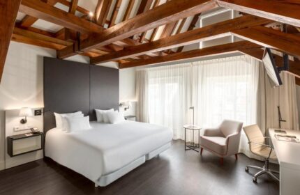 NH Collection Amsterdam Barbizon Palace room. Beams on ceiling, bed, desk, chair. Gay-friendly hotel in Amsterdam for gay men travel advice.