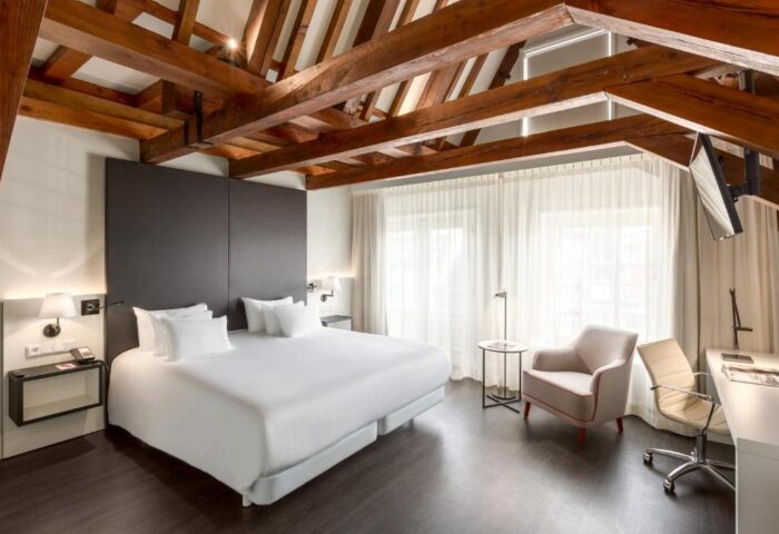 NH Collection Amsterdam Barbizon Palace room. Beams on ceiling, bed, desk, chair. Gay-friendly hotel in Amsterdam for gay men travel advice.