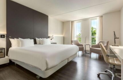 NH Collection Amsterdam Barbizon Palace's room. Gay-friendly hotel with a bed, chairs, desk, and windows. Modern interior design.