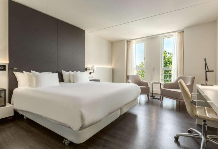 NH Collection Amsterdam Barbizon Palace's room. Gay-friendly hotel with a bed, chairs, desk, and windows. Modern interior design.