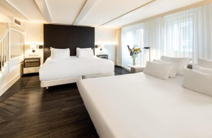 NH Collection Amsterdam Barbizon Palace gay-friendly hotel room. Modern design with white linens, dark wood floors, and staircase. Comfortable stay.
