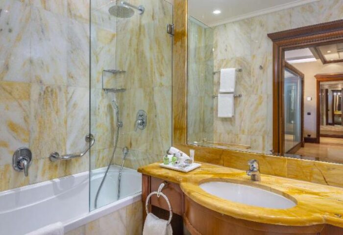 Bathroom at NH Collection Carlo IV, a gay-friendly, pet-friendly hotel. Features a bathtub, shower, marble walls, and a glimpse into the room.