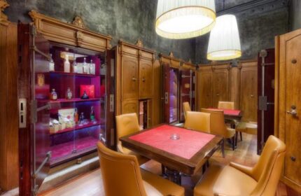 NH Collection Carlo IV gay-friendly hotel's unique bar area. Vault-like cabinets display liquor. Tables and chairs create an intimate setting.