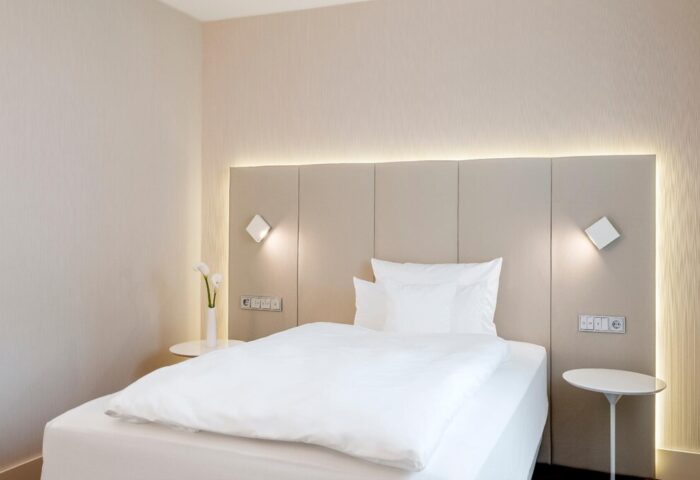 NH Collection Frankfurt City hotel room. Modern design with white linens, side tables, and sleek lighting. Gay-friendly hotel for travelers.