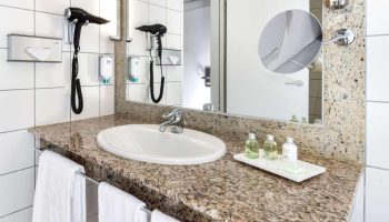 NH Collection Frankfurt City gay-friendly hotel bathroom. Sink, granite countertop, mirror, hair dryer, amenities, and white towels.