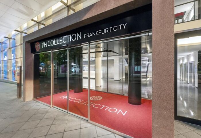 Entrance to the gay-friendly NH Collection Frankfurt City Hotel. Red carpet with the hotel logo welcomes guests. Modern architecture.