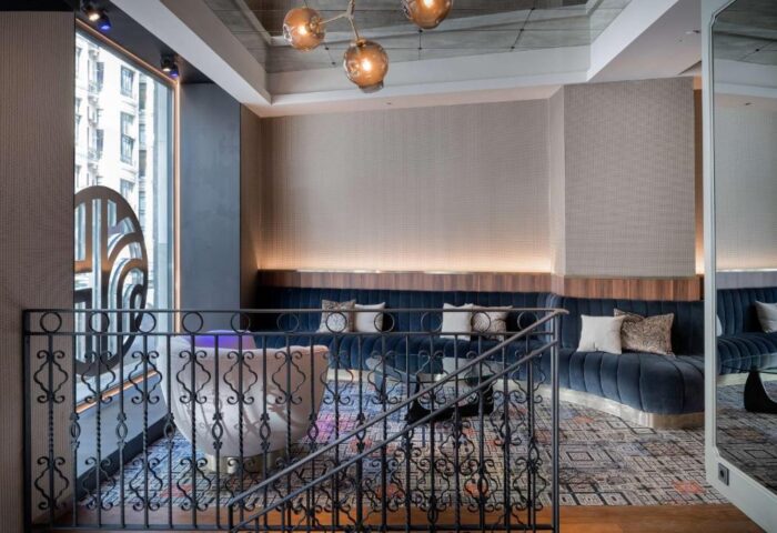 Interior of NH Collection Madrid Gran Via, a gay-friendly, pet-friendly hotel. Stylish lounge with blue velvet seating, patterned rug, and iron railing.