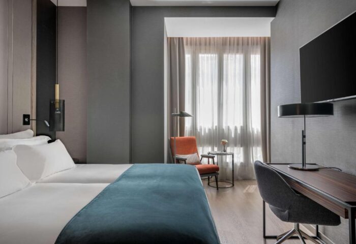 NH Collection Madrid Gran Via room. Gay-friendly, pet-friendly hotel room with desk, chair, bed, and window. Modern design, comfortable stay.