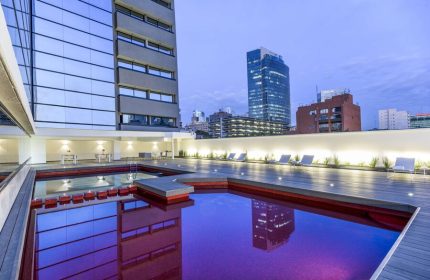 Rooftop pool at NH Collection Mexico City Reforma, a gay-friendly hotel. Loungers line the deck with city views. Building reflects in the water.