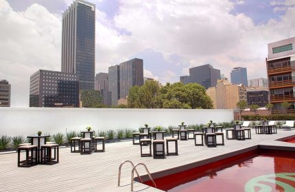 NH Collection Mexico City Reforma's gay-friendly rooftop pool area. Tables and stools line the deck, with Mexico City skyline views.