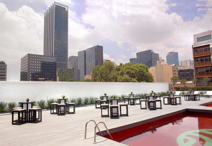 NH Collection Mexico City Reforma's gay-friendly rooftop pool area. Tables and stools line the deck, with Mexico City skyline views.
