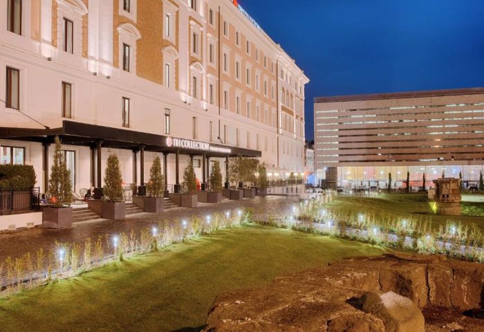 NH Collection Palazzo Cinquecento hotel exterior at night. Gay-friendly hotel with modern architecture, garden, and illuminated walkway. Rome travel.