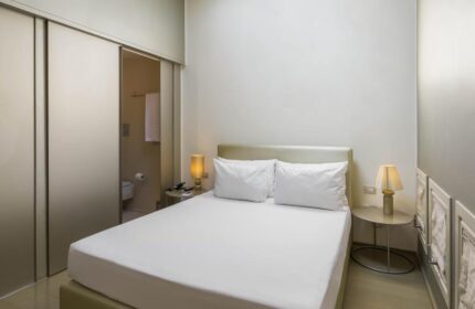 NH Milano Palazzo Moscova gay-friendly hotel room. Double bed with white linens, bedside tables with lamps, and bathroom view. Modern design.