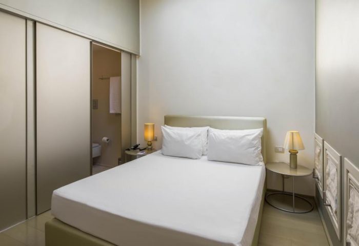 NH Milano Palazzo Moscova gay-friendly hotel room. Double bed with white linens, bedside tables with lamps, and bathroom view. Modern design.