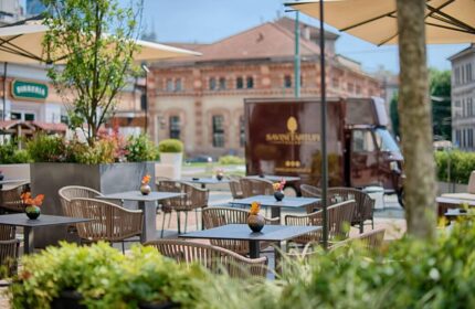 NH Milano Palazzo Moscova's outdoor dining area. Tables and chairs are set up on a patio, with umbrellas providing shade. Gay-friendly hotel.