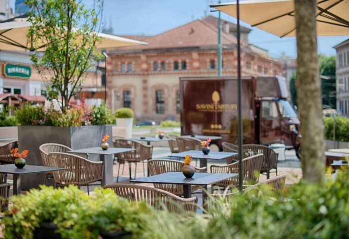 NH Milano Palazzo Moscova's outdoor dining area. Tables and chairs are set up on a patio, with umbrellas providing shade. Gay-friendly hotel.