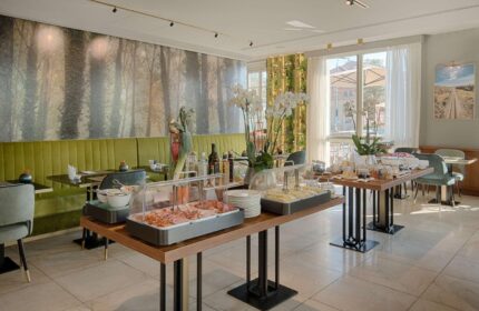Breakfast buffet at NH Milano Palazzo Moscova, a gay-friendly hotel. Food selection includes ham, cheese, and pastries. Modern design, bright space.