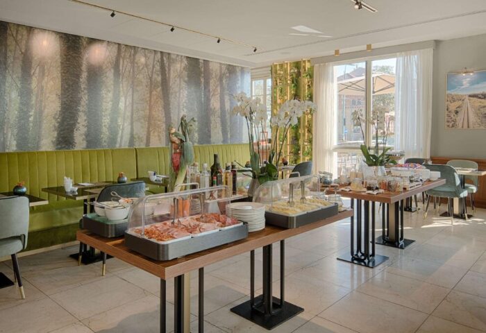 Breakfast buffet at NH Milano Palazzo Moscova, a gay-friendly hotel. Food selection includes ham, cheese, and pastries. Modern design, bright space.