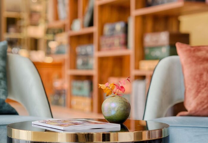 Cozy lounge at NH Milano Palazzo Moscova, a gay-friendly hotel. Table with a vase and magazine, chairs, and a bookshelf in the background.