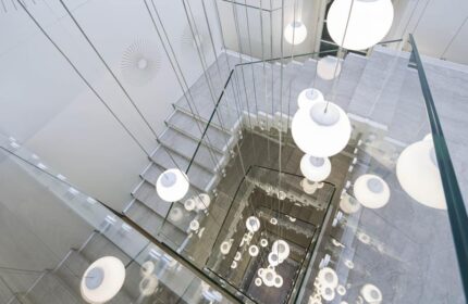 Stairwell at NH Milano Palazzo Moscova, a gay-friendly hotel. Modern design with glass railings and hanging globe lights. Chic Milan hotel.