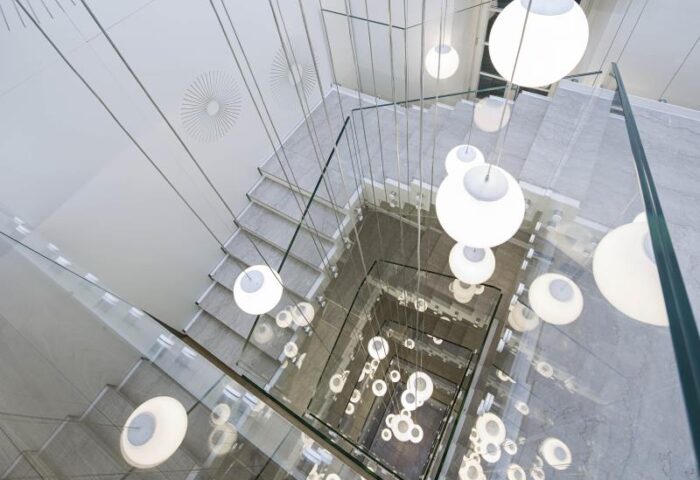 Stairwell at NH Milano Palazzo Moscova, a gay-friendly hotel. Modern design with glass railings and hanging globe lights. Chic Milan hotel.