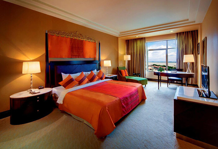NagaWorld Hotel & Entertainment Complex room. Gay-friendly hotel featuring a bed with orange bedding, desk, and city view. Gay travel advice.