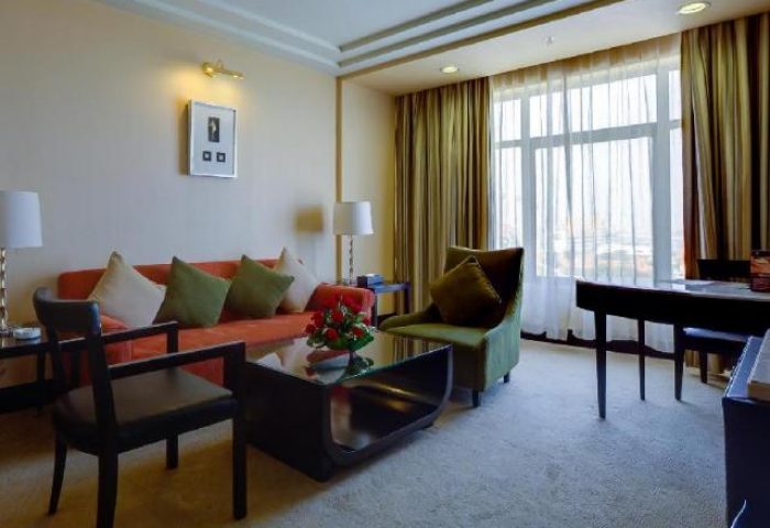 NagaWorld Hotel & Entertainment Complex suite. Gay-friendly hotel living area with sofa, chair, desk, and large window.