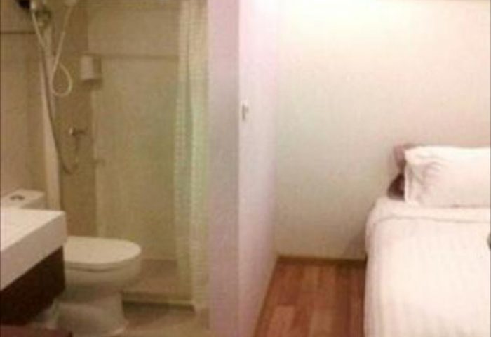 Nantra Silom Hotel room. Gay-friendly hotel bathroom with shower, toilet, and sink. Bedroom area with bed and white linens. Bangkok hotel.