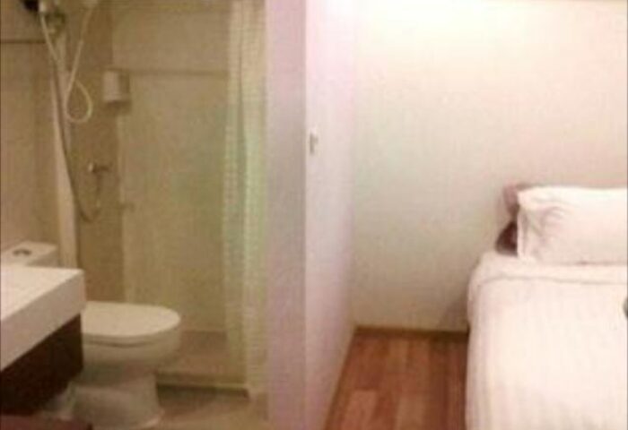 Nantra Silom Hotel room. Gay-friendly hotel bathroom with shower, toilet, and sink. Bedroom area with bed and white linens. Bangkok hotel.