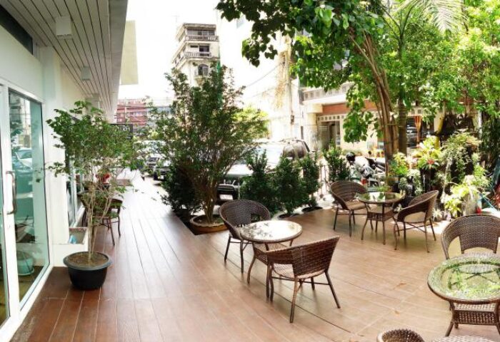 Outdoor seating area at Nantra Silom Hotel, a gay-friendly hotel. Features tables, chairs, and lush greenery. Silom, Bangkok.