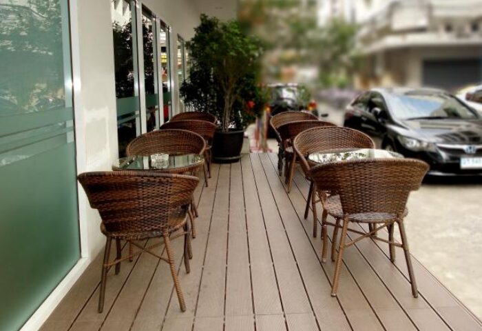 Outdoor seating at Nantra Silom Hotel, a gay-friendly hotel in Bangkok. Wicker chairs and glass-topped tables line the wooden deck.