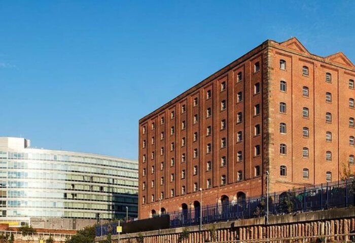 Native Manchester Gay-Friendly Hotel: Exterior view of the hotel, a red brick building, next to a modern glass building. Blue sky in the background.