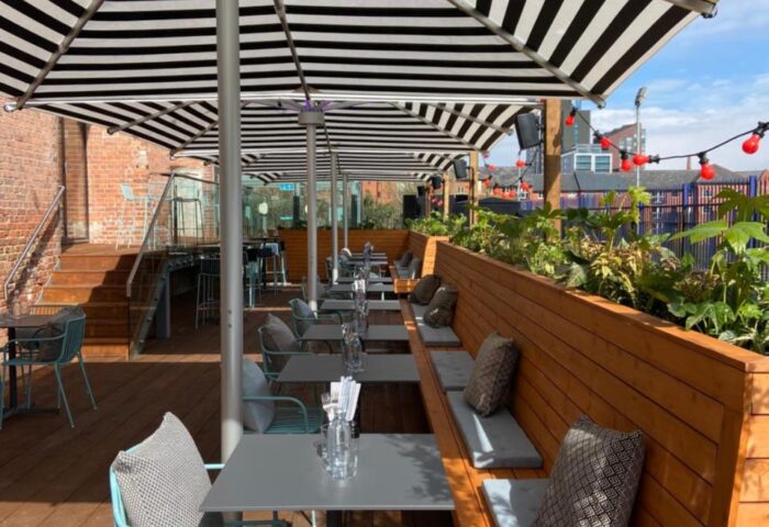 Native Manchester gay-friendly hotel outdoor seating area. Tables and chairs under striped umbrellas, perfect for gay travelers in Manchester.